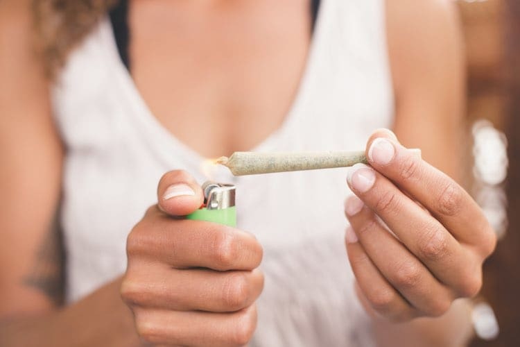 Person holding a lit joint with a green lighter in a lifestyle scene